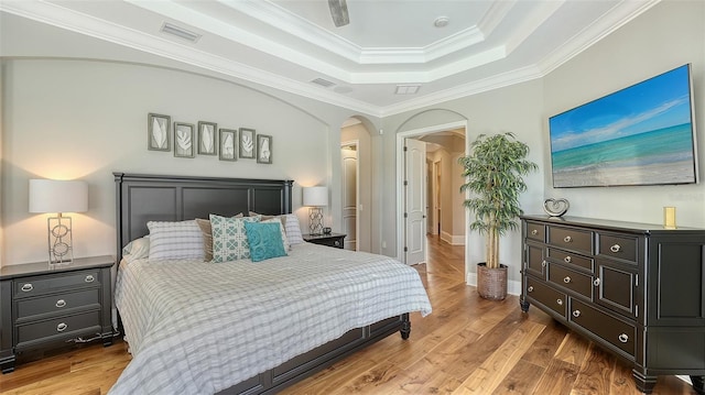 bedroom with a tray ceiling, arched walkways, visible vents, ornamental molding, and wood finished floors