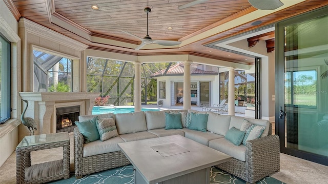 sunroom / solarium featuring ceiling fan, wood ceiling, a lit fireplace, a raised ceiling, and decorative columns