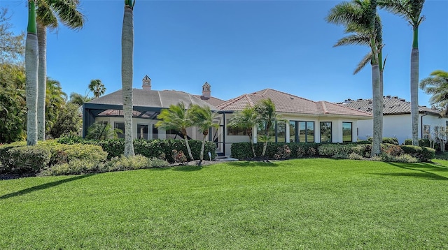 mediterranean / spanish home with a lanai, a tiled roof, a front lawn, and stucco siding