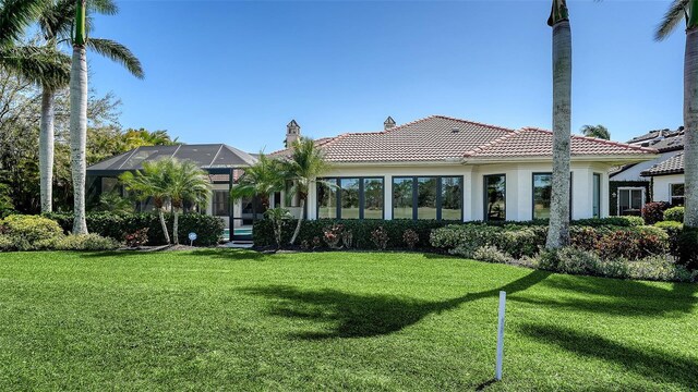 back of house featuring a tiled roof, a lawn, and a lanai