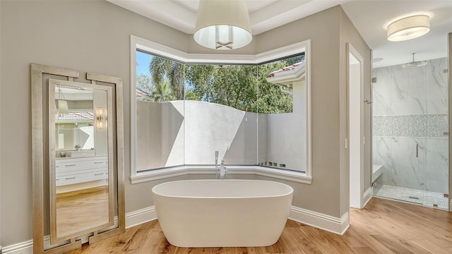 bathroom with a freestanding bath, wood finished floors, a marble finish shower, and baseboards