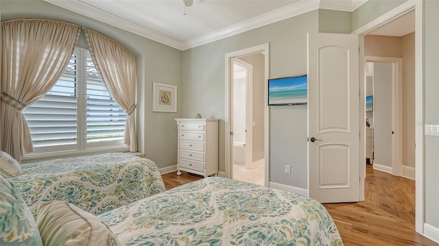 bedroom featuring baseboards, ensuite bathroom, wood finished floors, and crown molding