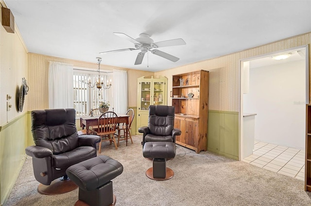 living area featuring tile patterned floors, wallpapered walls, wainscoting, carpet flooring, and ceiling fan with notable chandelier