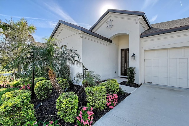 entrance to property with a garage, roof with shingles, driveway, and stucco siding