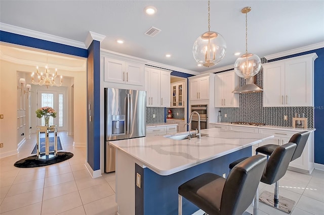 kitchen with an island with sink, glass insert cabinets, stainless steel appliances, white cabinetry, and a sink