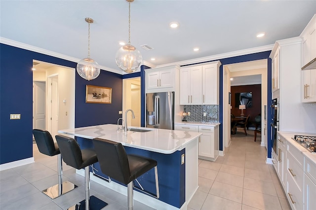 kitchen with decorative light fixtures, light countertops, appliances with stainless steel finishes, white cabinets, and a kitchen island with sink