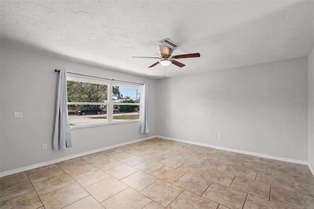 empty room with a textured ceiling, visible vents, a ceiling fan, and baseboards