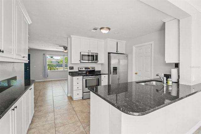 kitchen featuring light tile patterned floors, a peninsula, a sink, white cabinets, and appliances with stainless steel finishes