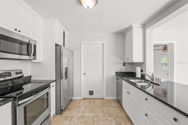 kitchen with dark stone counters, a ceiling fan, appliances with stainless steel finishes, white cabinetry, and a sink