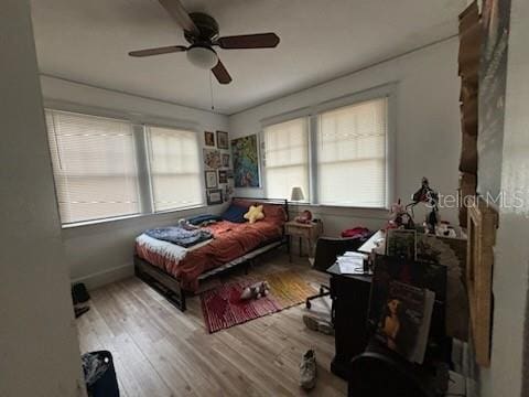 bedroom featuring ceiling fan, multiple windows, baseboards, and wood finished floors