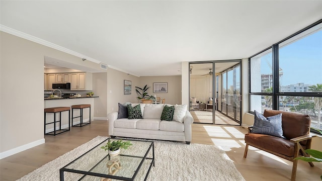 living room featuring visible vents, baseboards, light wood finished floors, a wall of windows, and crown molding