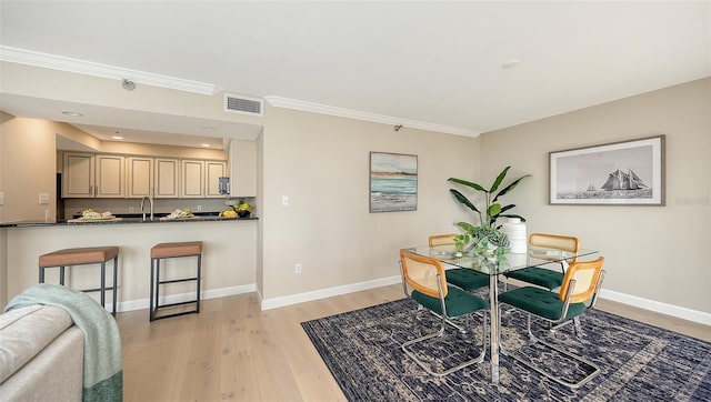 dining room featuring light wood-style flooring, visible vents, baseboards, and crown molding