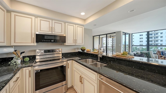 kitchen featuring cream cabinets, recessed lighting, a sink, appliances with stainless steel finishes, and dark stone counters