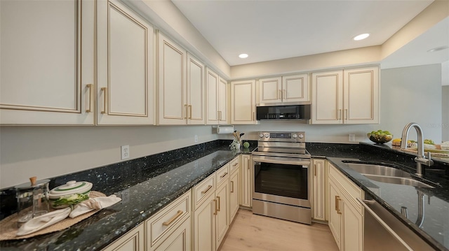 kitchen with stainless steel appliances, a sink, light wood finished floors, and cream cabinets