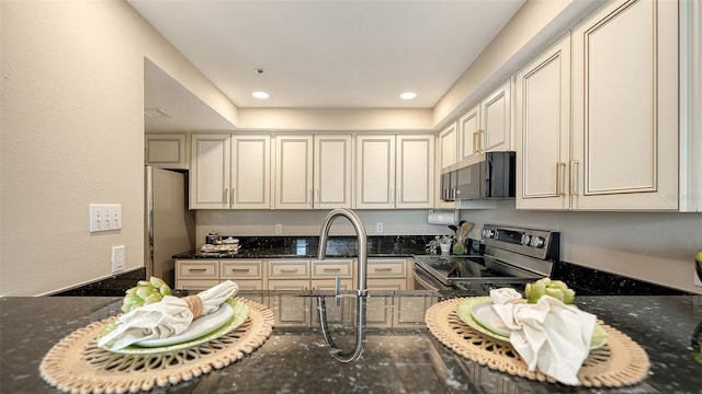 kitchen with appliances with stainless steel finishes, dark stone counters, cream cabinetry, and recessed lighting