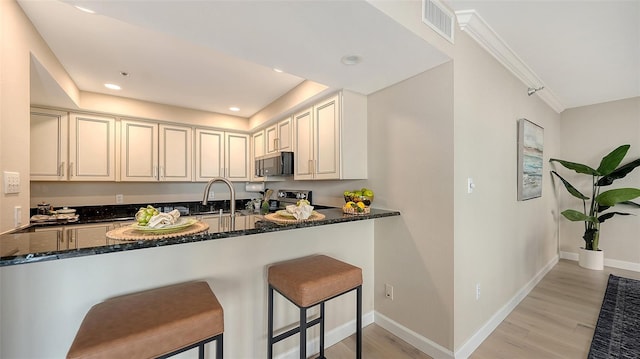 kitchen with a peninsula, light wood-type flooring, appliances with stainless steel finishes, and dark stone counters