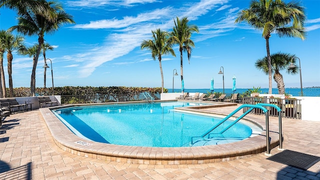 pool with a patio area, fence, and a water view