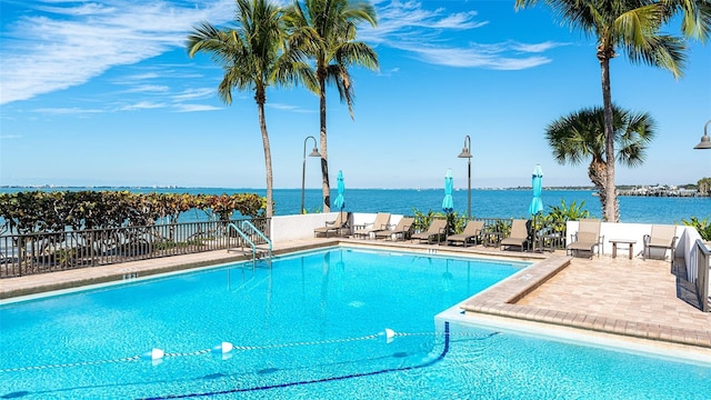 pool featuring a patio, a water view, and fence