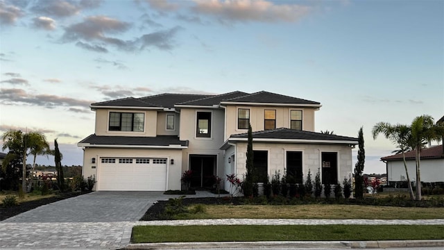 prairie-style house featuring an attached garage, a front lawn, decorative driveway, and stucco siding