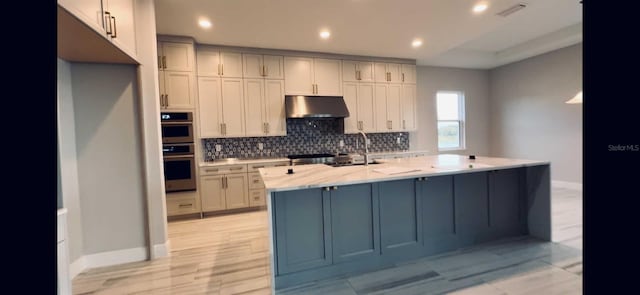 kitchen with light countertops, visible vents, decorative backsplash, a sink, and under cabinet range hood