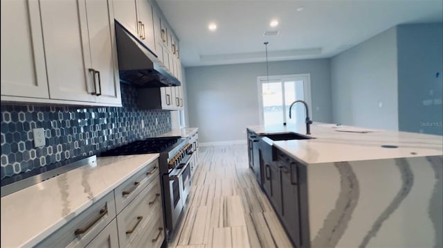 kitchen with light stone counters, decorative backsplash, a sink, double oven range, and under cabinet range hood