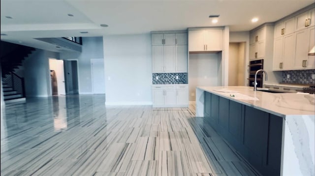 kitchen featuring tasteful backsplash, open floor plan, light stone countertops, stainless steel double oven, and a sink