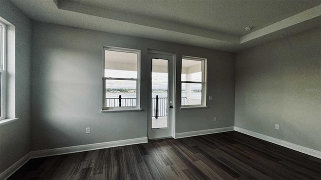 unfurnished room with dark wood-style floors, a tray ceiling, and baseboards