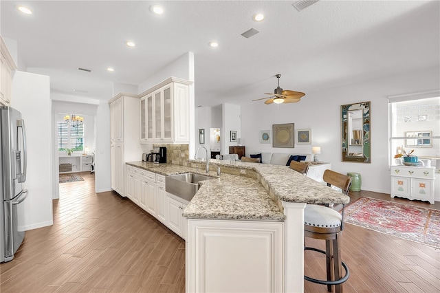 kitchen with a peninsula, ceiling fan, a sink, stainless steel refrigerator with ice dispenser, and a kitchen bar