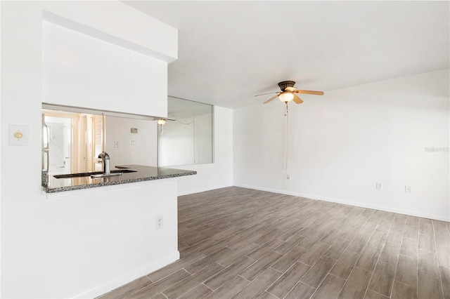 unfurnished living room featuring ceiling fan, baseboards, a sink, and wood finished floors