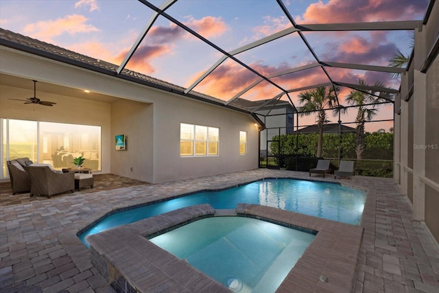 pool at dusk featuring a patio, a lanai, outdoor lounge area, a pool with connected hot tub, and a ceiling fan