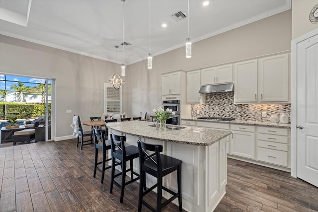 kitchen featuring dark wood finished floors, tasteful backsplash, visible vents, ornamental molding, and under cabinet range hood