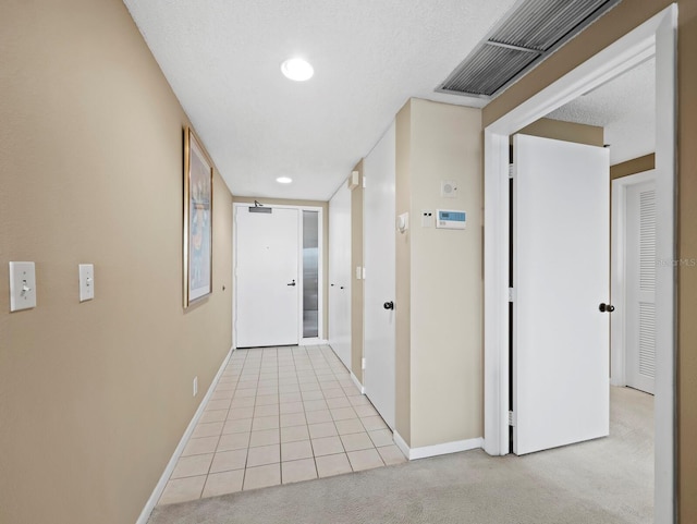 hallway featuring light carpet, visible vents, baseboards, and a textured ceiling