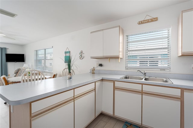 kitchen featuring visible vents, light countertops, open floor plan, a sink, and a peninsula