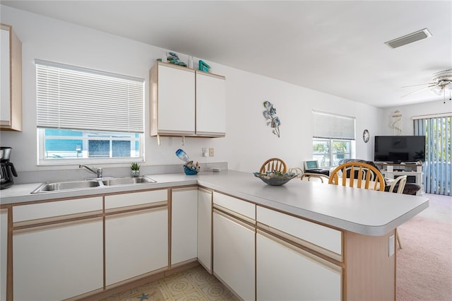 kitchen with light countertops, visible vents, open floor plan, a sink, and a peninsula