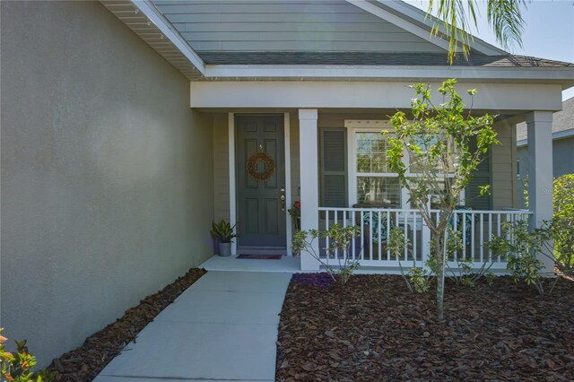 view of exterior entry with stucco siding, a porch, and roof with shingles