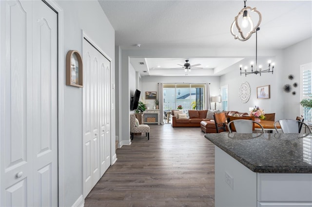 kitchen with dark wood-type flooring, baseboards, decorative light fixtures, a tray ceiling, and dark stone countertops