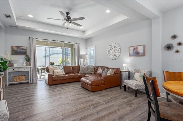 living area featuring visible vents, a raised ceiling, a ceiling fan, and wood finished floors