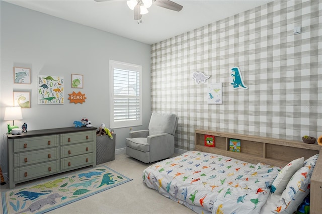 carpeted bedroom with wallpapered walls, an accent wall, and a ceiling fan