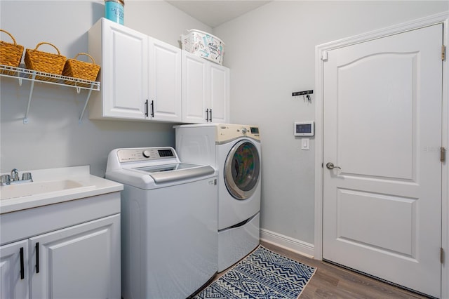 laundry area featuring dark wood-type flooring, baseboards, cabinet space, independent washer and dryer, and a sink