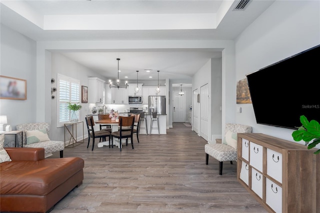 living room featuring a notable chandelier, wood finished floors, visible vents, and baseboards