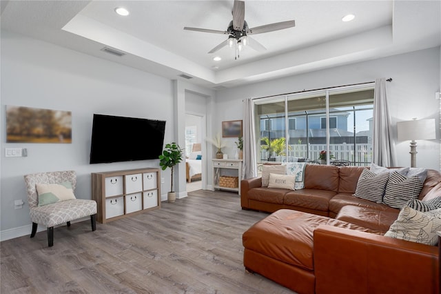 living room with a raised ceiling, plenty of natural light, wood finished floors, and visible vents