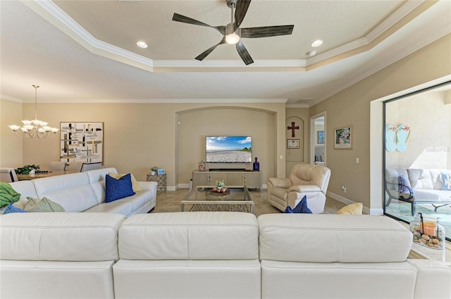 living room with baseboards, a tray ceiling, crown molding, and ceiling fan with notable chandelier