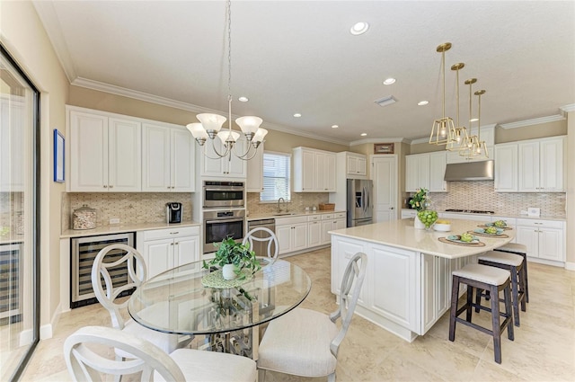 kitchen with wine cooler, appliances with stainless steel finishes, white cabinetry, a sink, and a kitchen breakfast bar