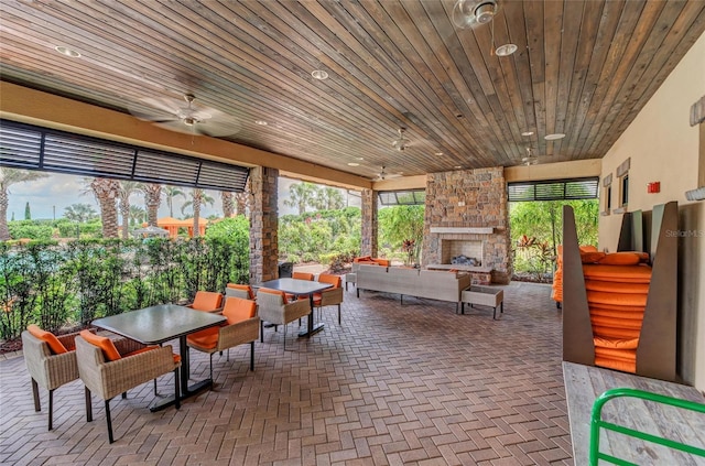 sunroom featuring wooden ceiling, ceiling fan, and an outdoor stone fireplace