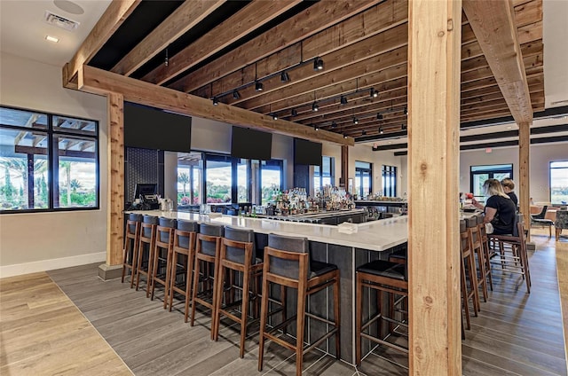 bar with rail lighting, wood finished floors, visible vents, and baseboards