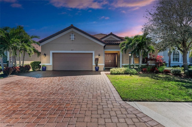 view of front of property featuring decorative driveway, a tile roof, stucco siding, a front yard, and a garage