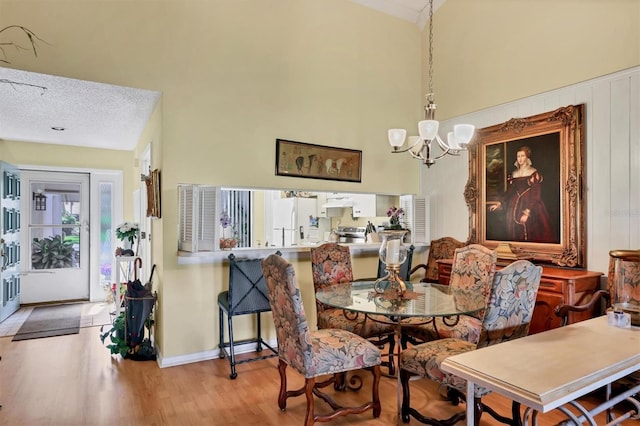 dining space with a notable chandelier, a textured ceiling, baseboards, and wood finished floors