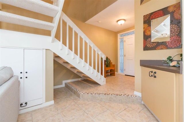 foyer entrance featuring stairs, light tile patterned floors, and baseboards