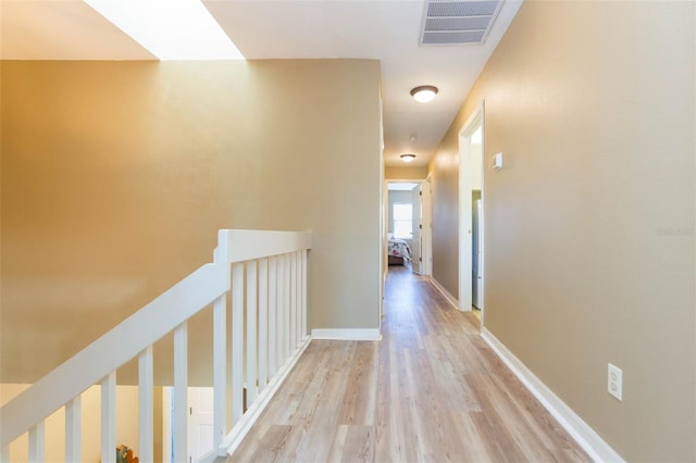 hall with light wood-style floors, baseboards, visible vents, and an upstairs landing