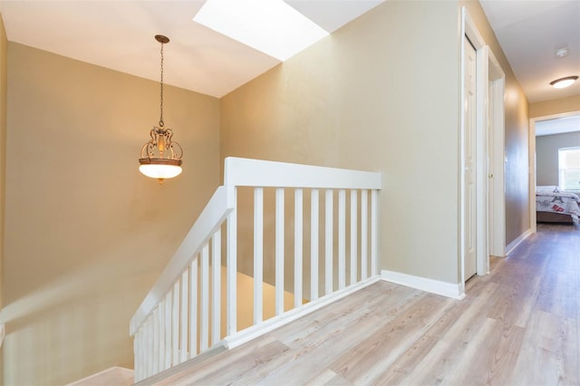 corridor with a skylight, wood finished floors, an upstairs landing, and baseboards